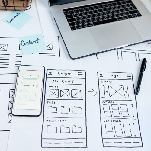 Hand-drawn wireframes on a desk with a pen and laptop